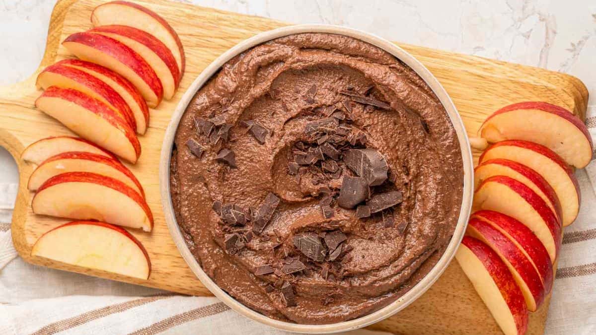 Chocolate Hummus served in a bowl with a few pieces of sliced apples. 