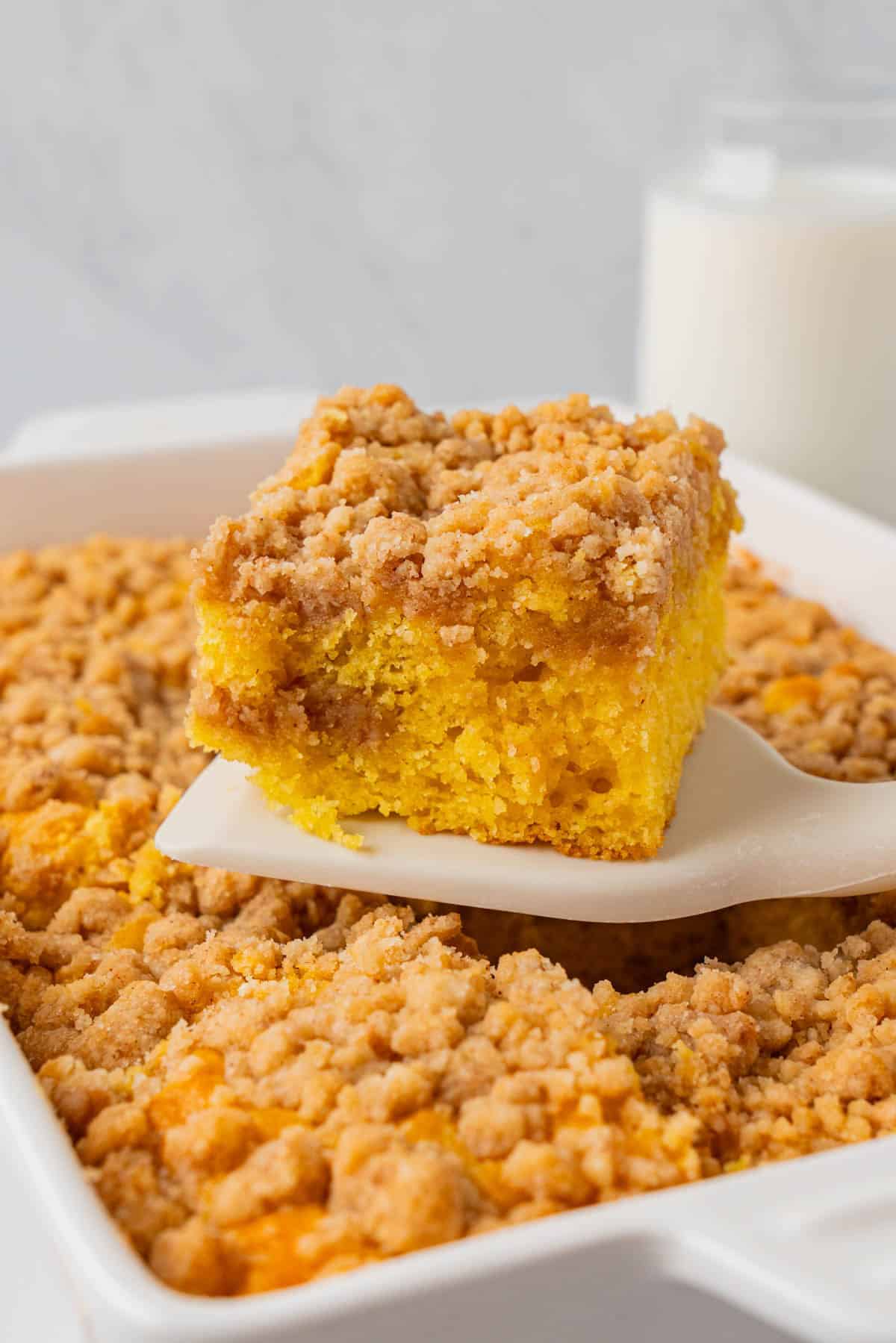 A slice of Cake Mix Coffee Cake With Yellow Cake taken from the casserole dish using a white spatula. 
