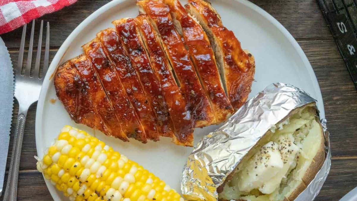 A serving of Air Fryer BBQ Chicken with corn on cob and baked potato.
