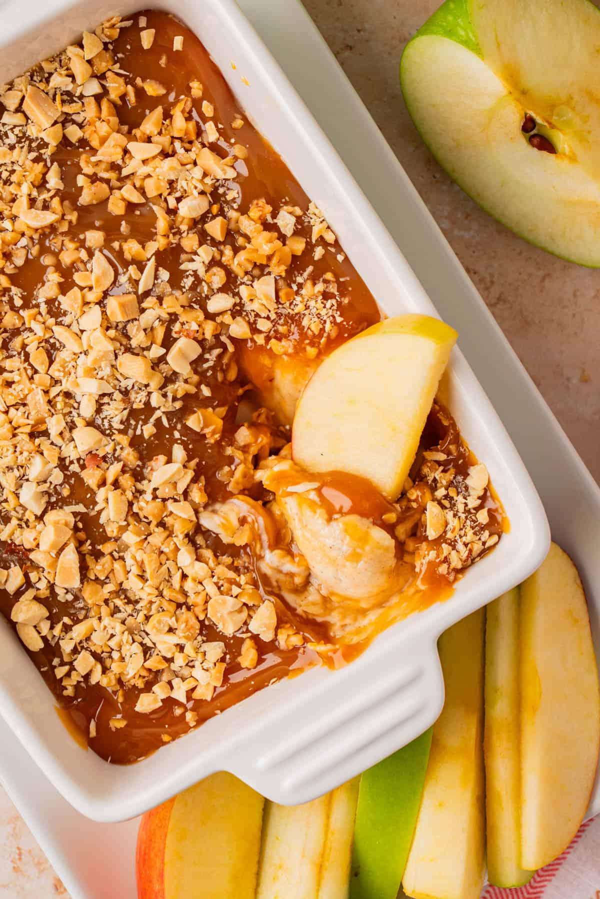 dish with Caramel Apple Cream Cheese Dip topped with crushed nuts and apple slices