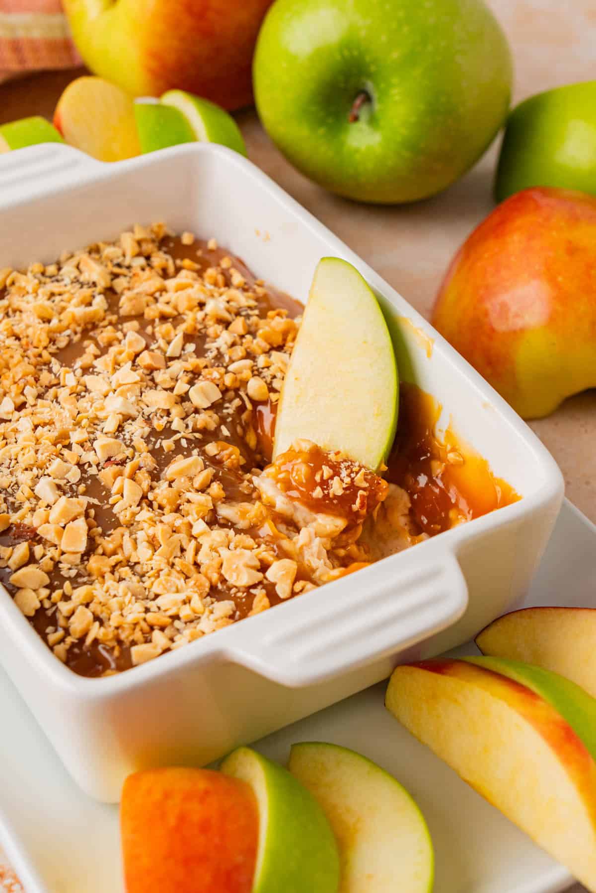 Caramel apple cream cheese dip in a casserole with sliced apple dip on it.