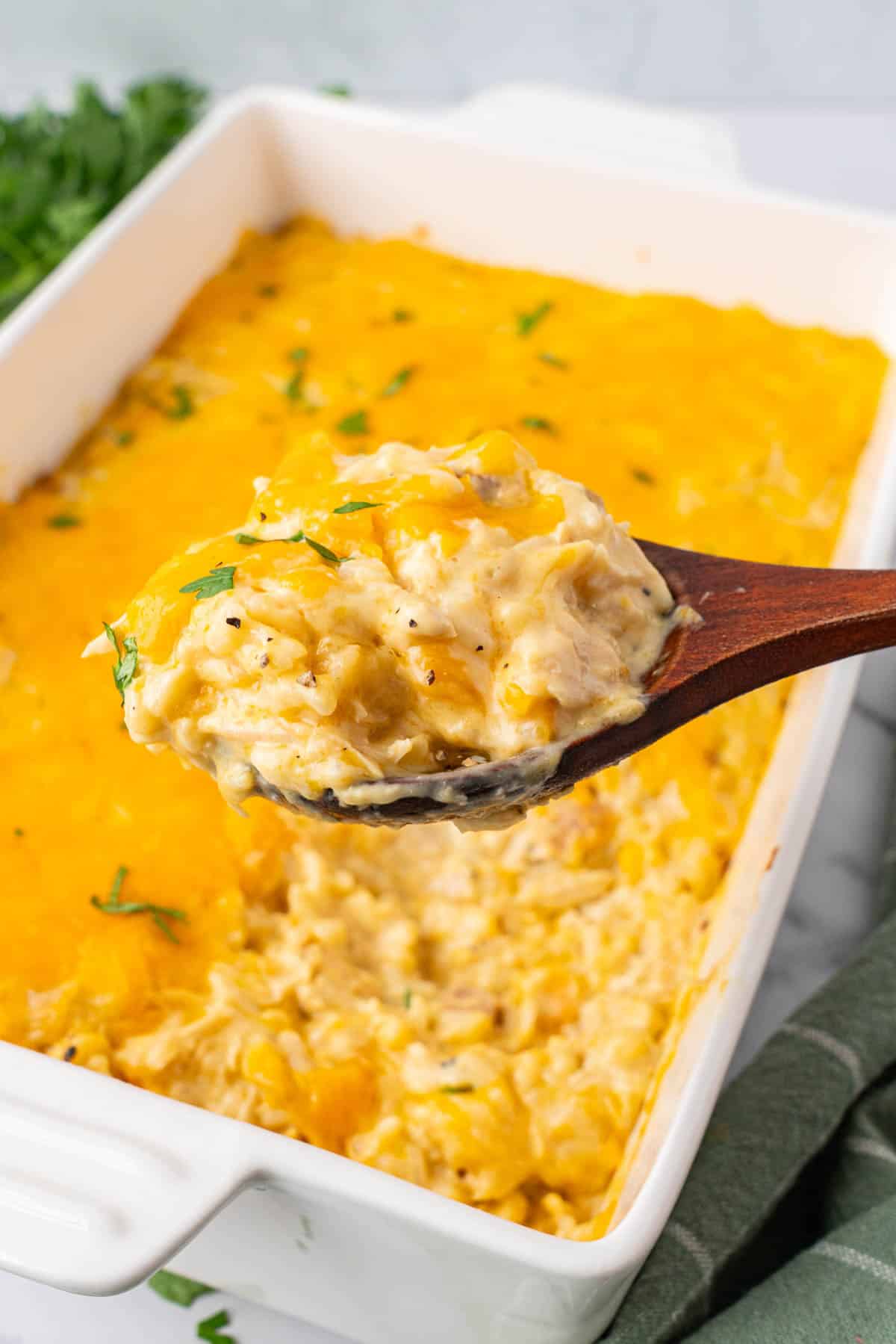 A scooped serving of Cheesy Chicken and Rice Casserole, a blurry background of Cheesy Chicken and Rice Casserole served in a baking dish. 