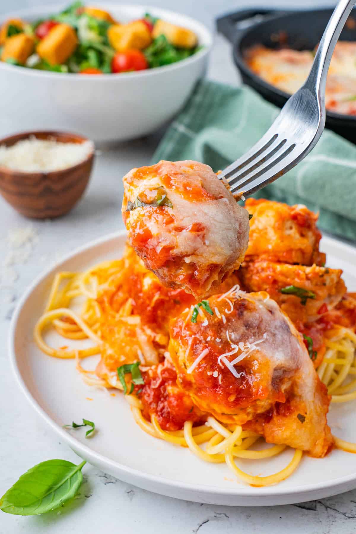 Cheesy Chicken and Rice Casserole Meatballs, served over pasta in a plate. A singular piece of meatball in the fork.