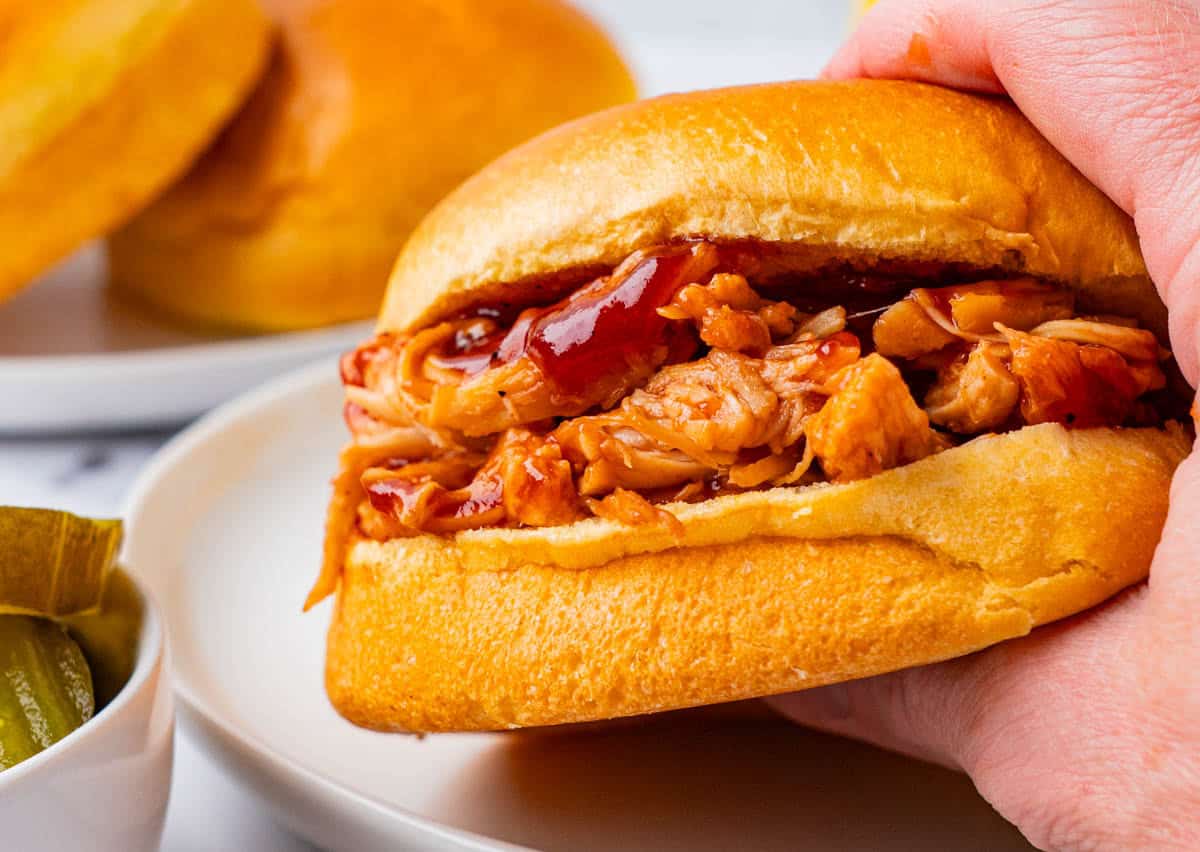 Close-up shot crockpot BBQ Pulled Chicken Sandwich held in hand.