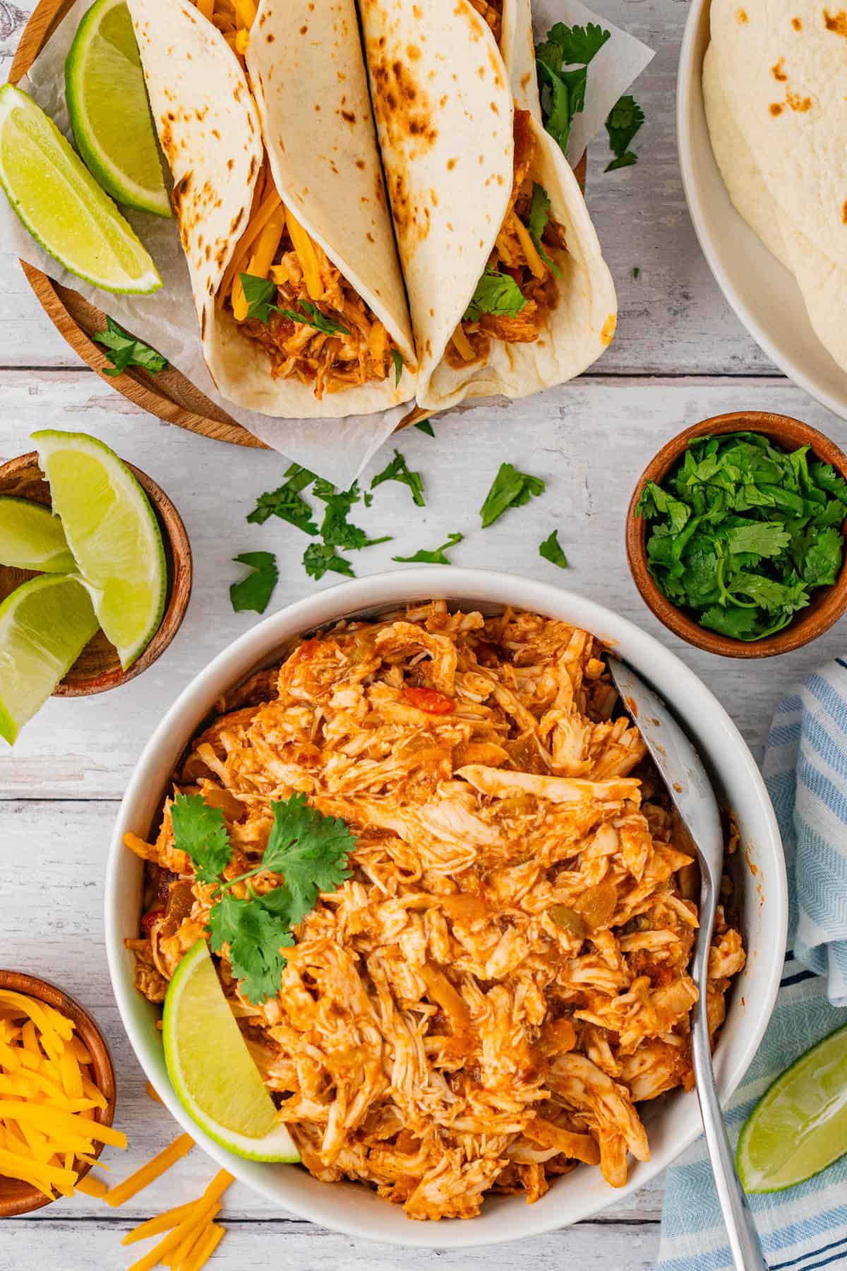 Crockpot Taco Chicken in a bowl, two Taco Chicken served in a wooden plate with slices of lime.