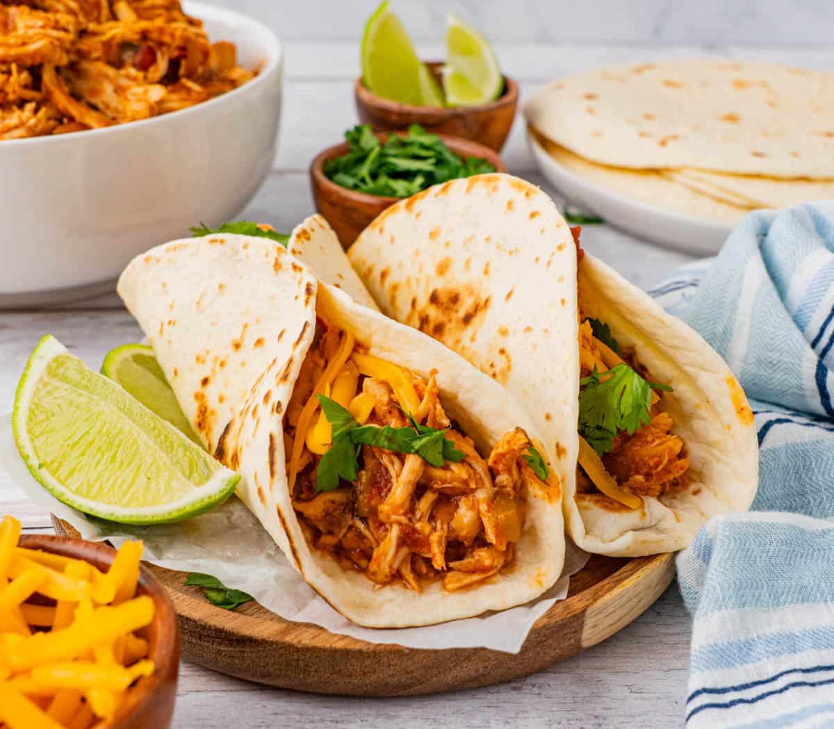 Two chicken tacos served on a wooden plate with two slices of lime.