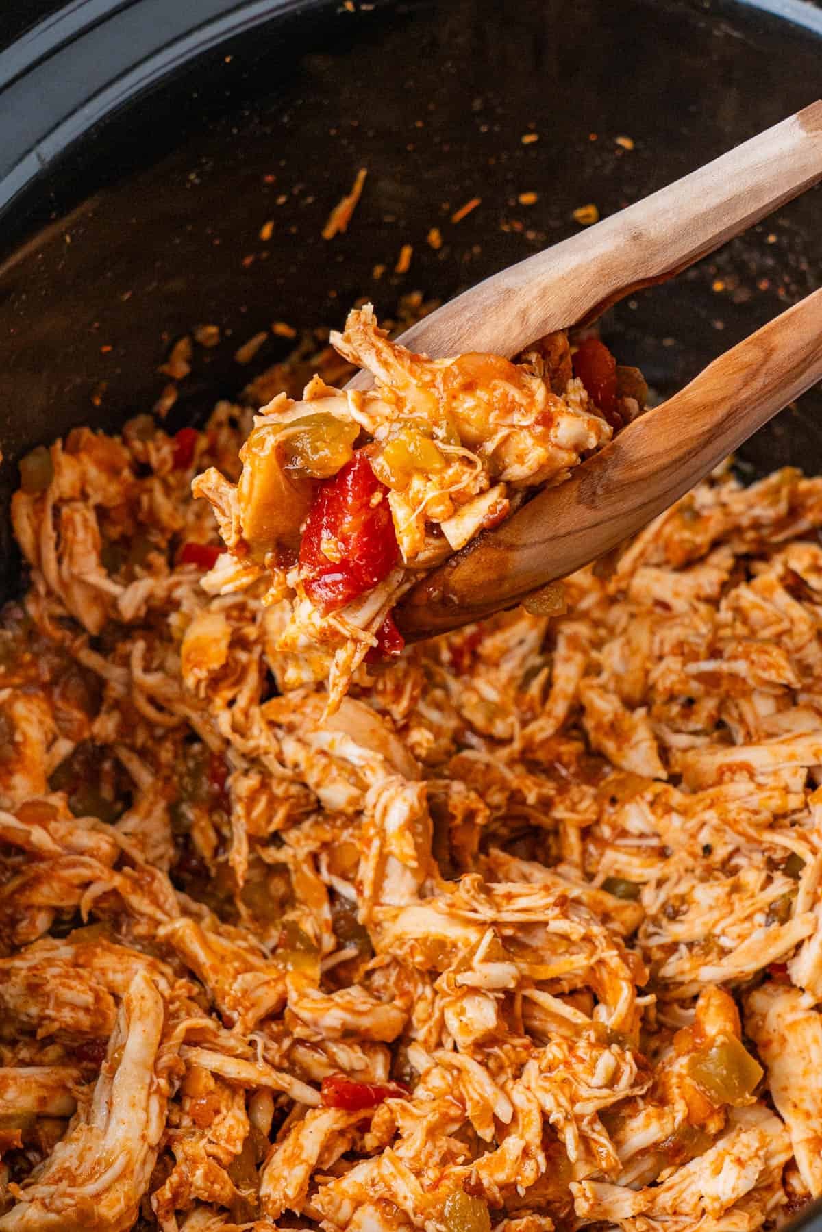 Wooden thongs with shredded Mexican Chicken in a crockpot.