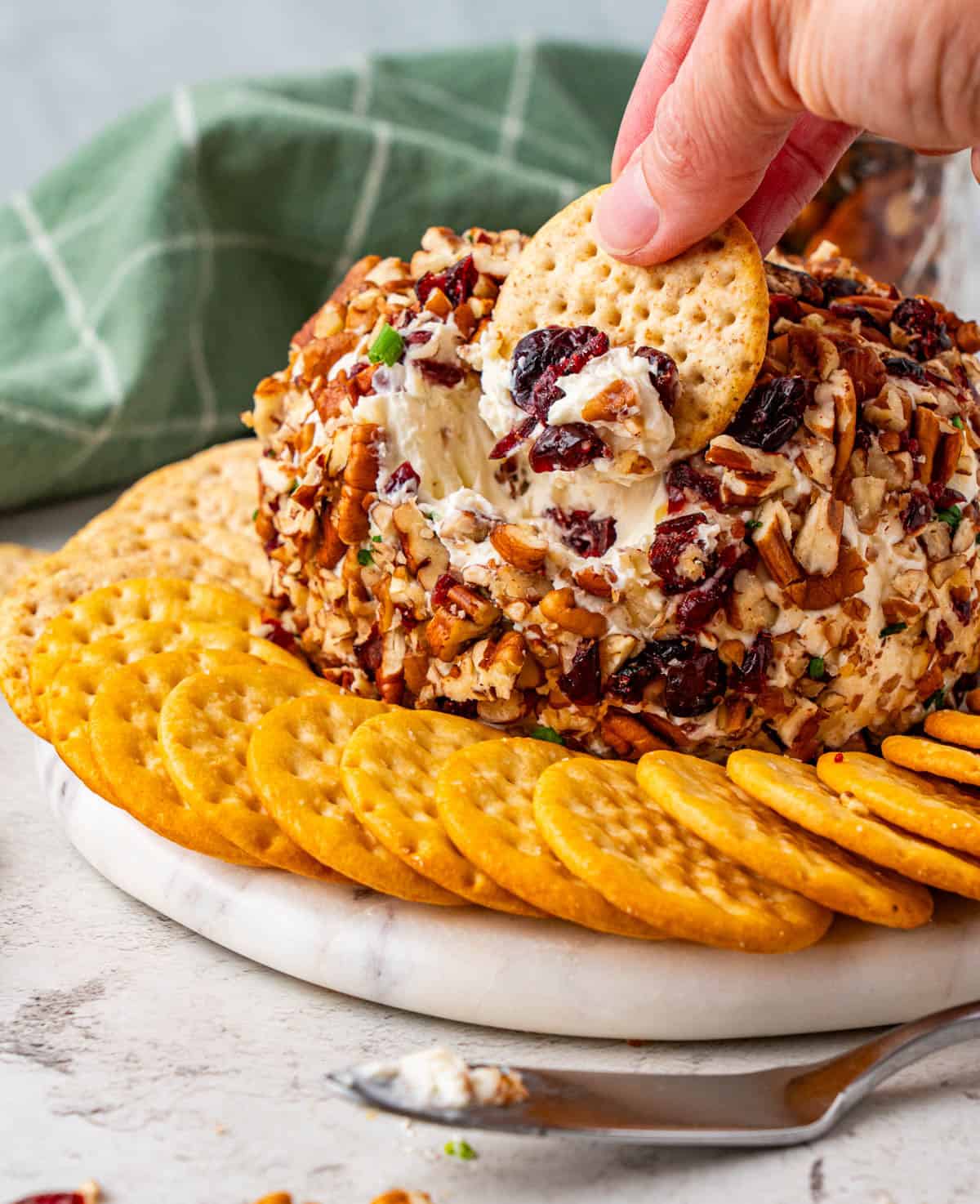 A hand dipping a cracker on the Cranberry Pecan Cheese Ball
