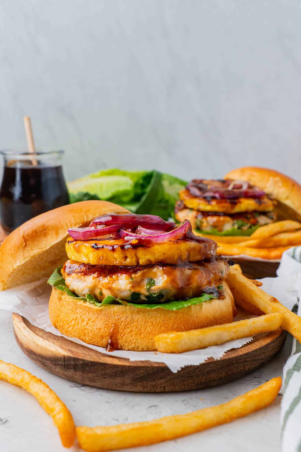 Teriyaki Chicken Burgers With Grilled Pineapple served in a wooden plate, with fries on the side. 