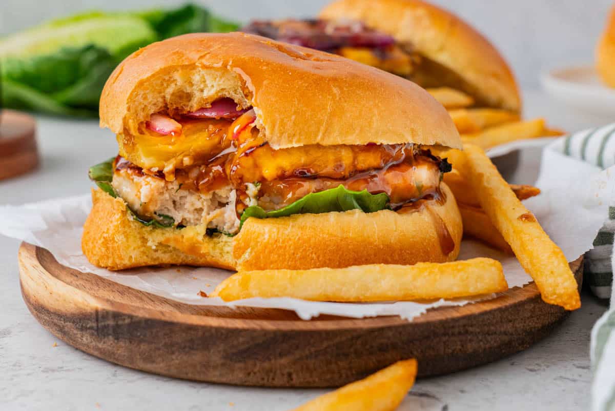 A serving of Teriyaki Chicken Burgers With Grilled Pineapple that was bit on served on a wooden plate 