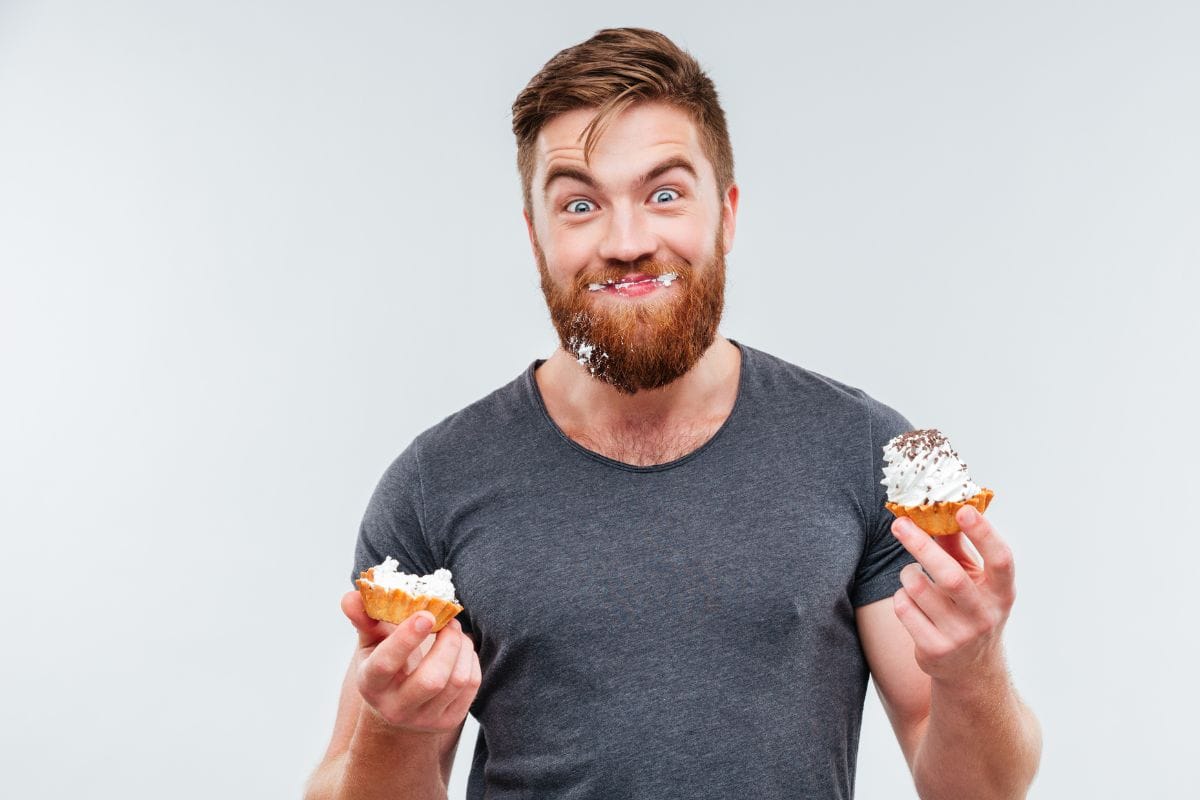 Man eating cupcakes with icing on his face 