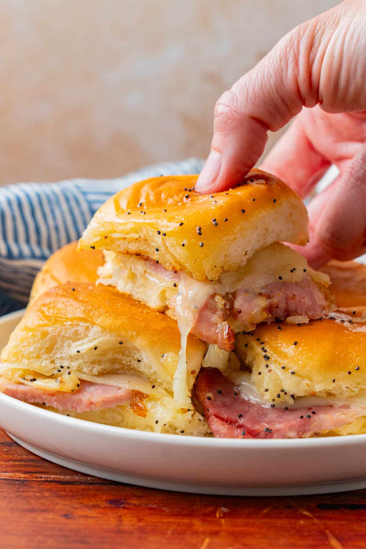 A hand grabbing a piece of Ham And Cheese Sliders on Hawaiian Rolls