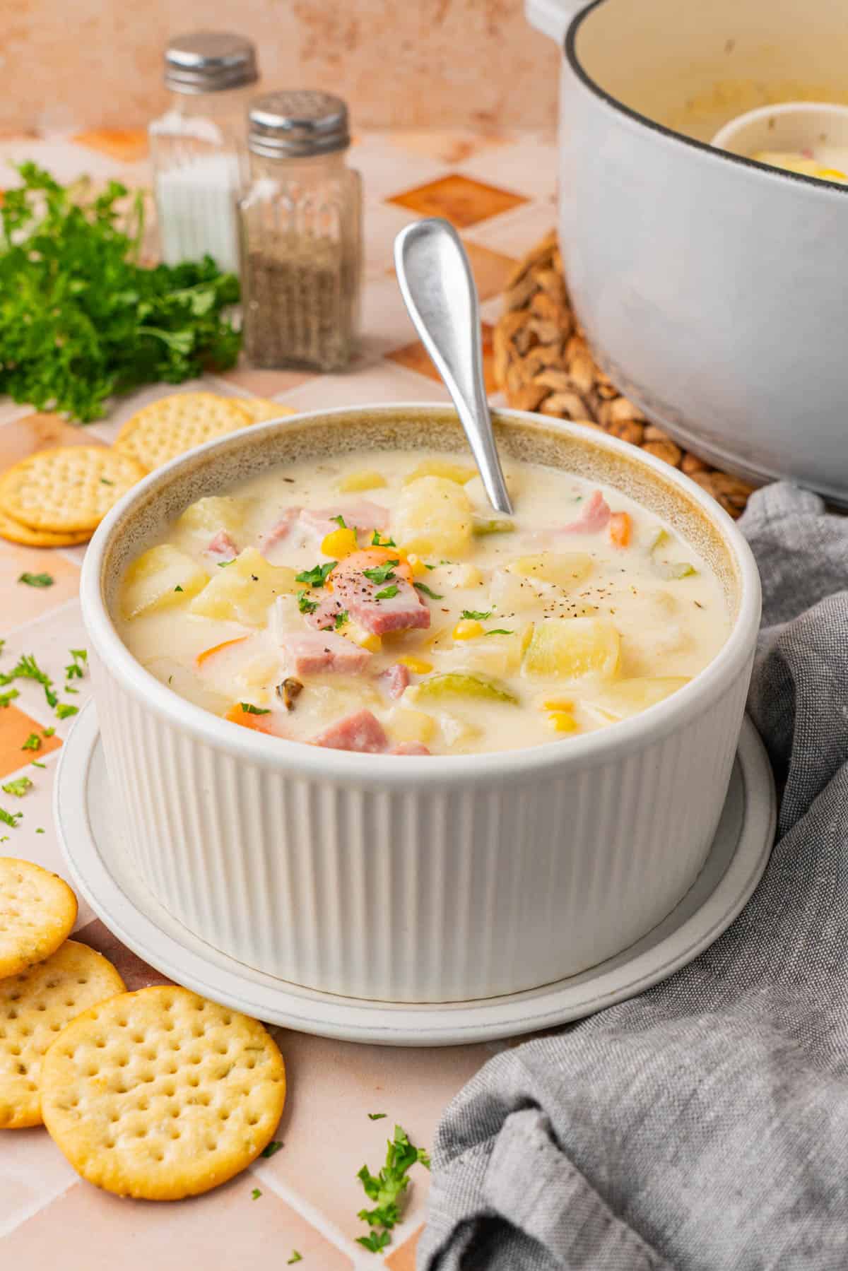 Creamy Ham And Potato Soup served on a bowl with a saucer and a spoon, a few biscuits is found from the sides.