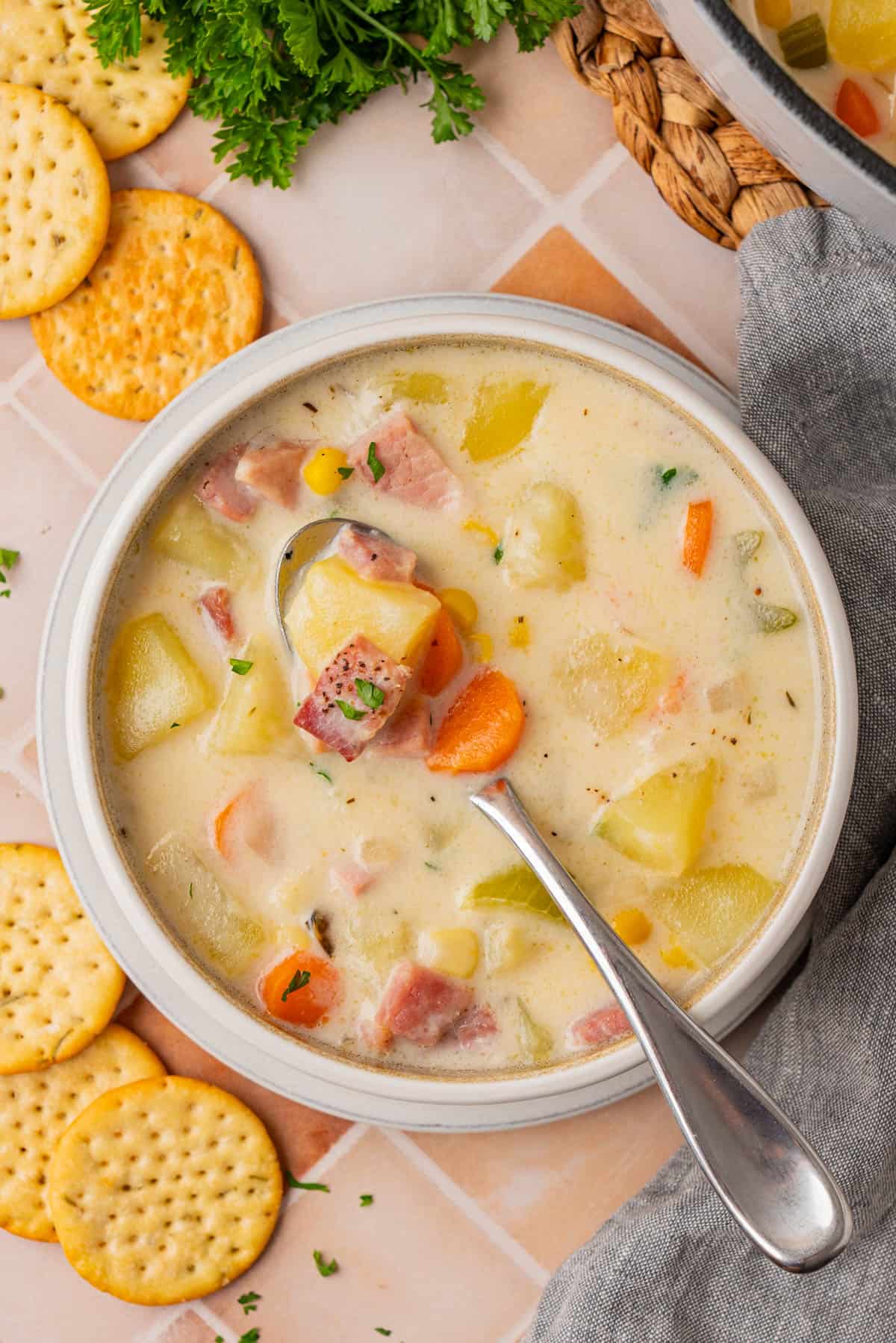 Creamy Ham And Potato Soup served in a bowl with a spoon, a few pieces of biscuits found on the side.
