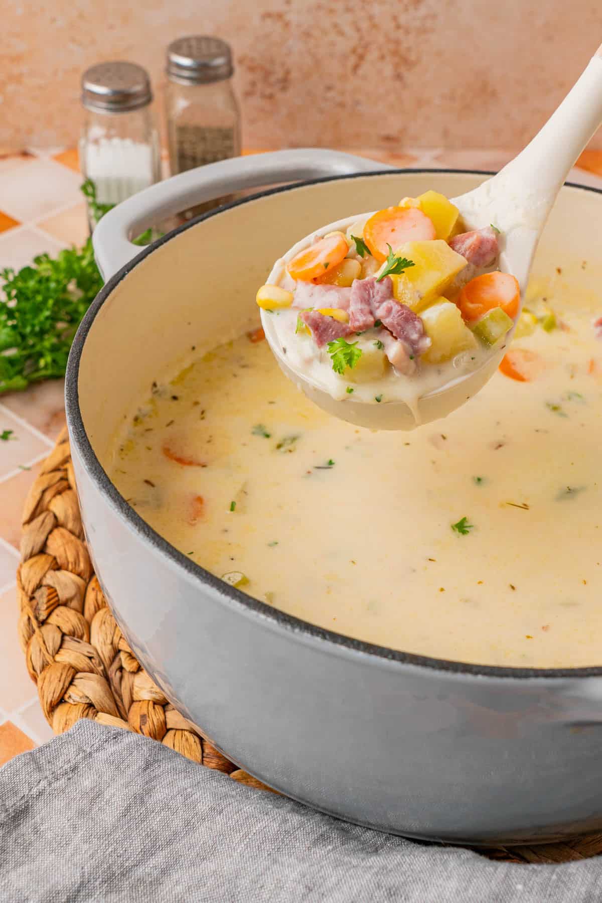 A ladle scooped out from the pot filled with Creamy Ham And Potato Soup.