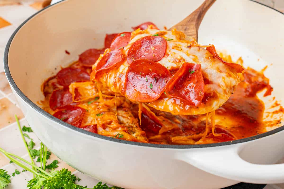 A serving of Low Carb Pizza Chicken scooped from the skillet using a wooden spatula.