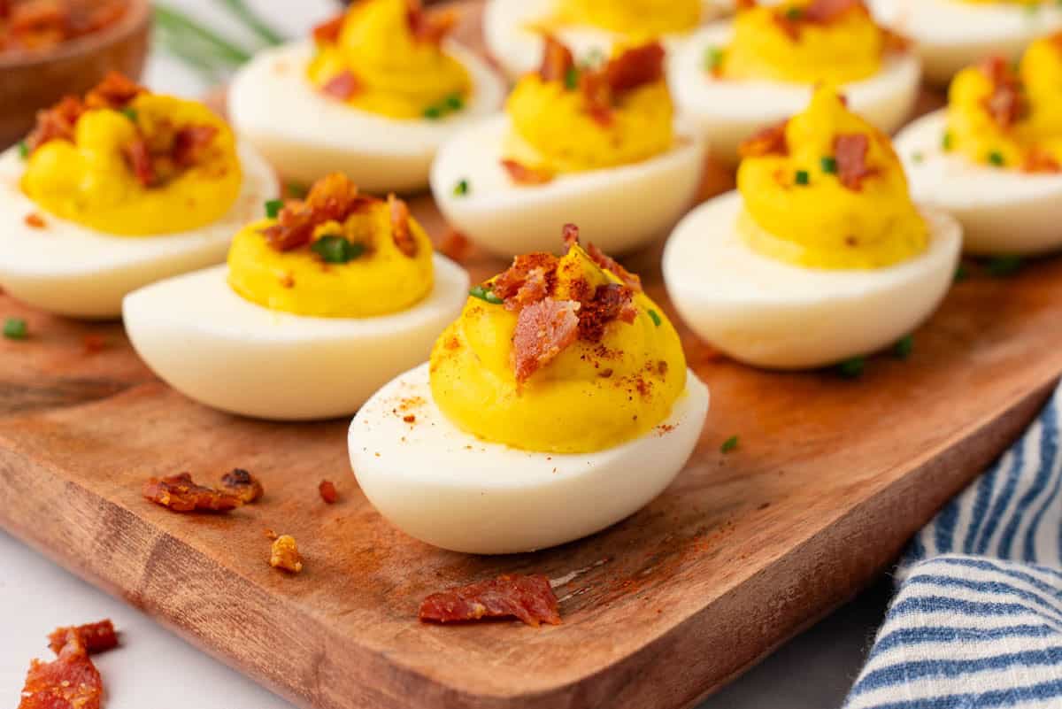 arranged deviled eggs with bacon in a wooden tray with crumbs of bacon in the tray.