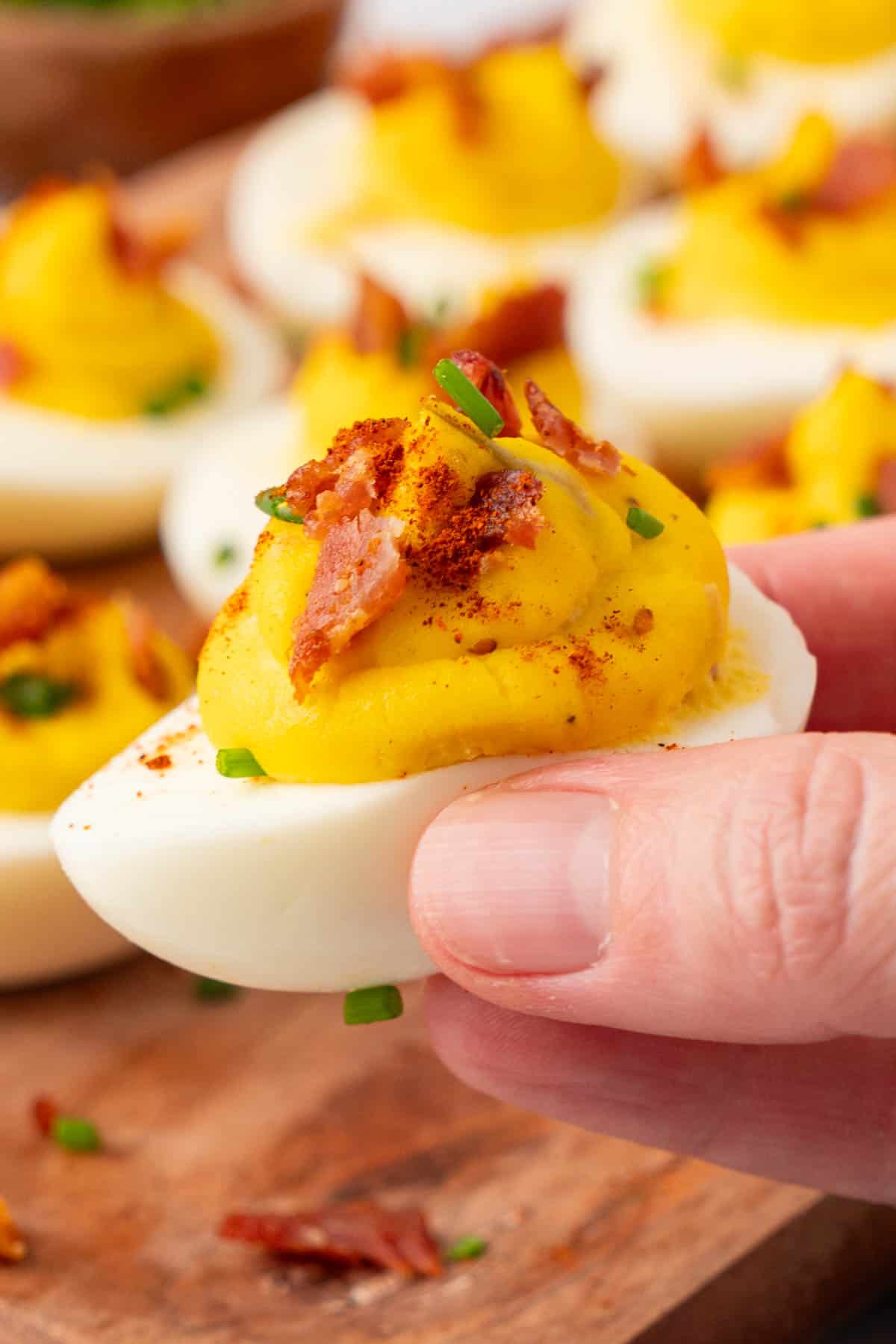 a hand holding a deviled eggs with bacon.