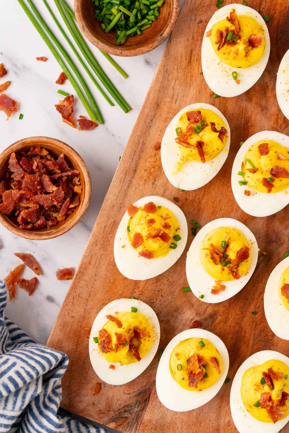 overhead shot of deviled eggs with bacon in a wooden serving tray with a bowl of bacon crumbs.