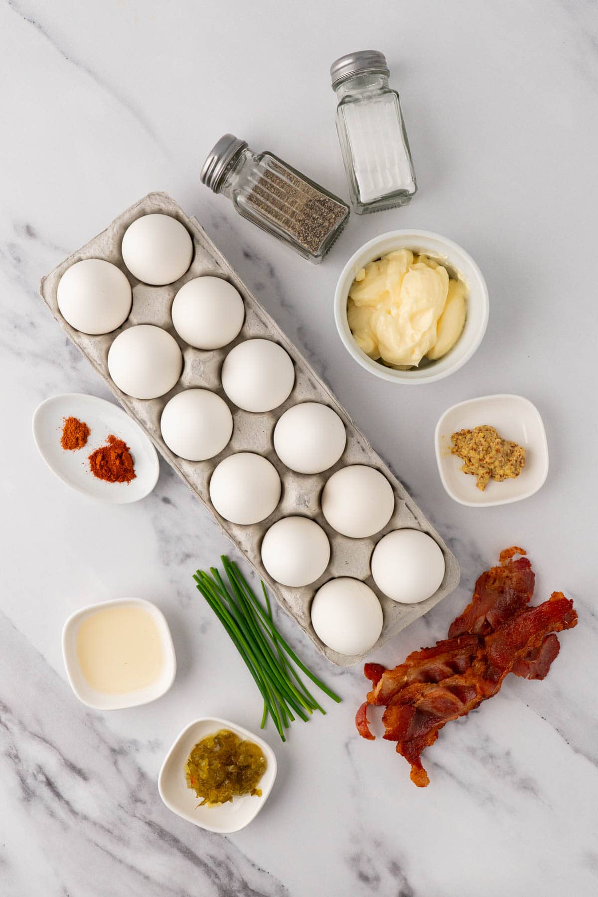 ingredients for deviled eggs with bacon are eggs, mayo, seasoning, mustard, cooked bacon, pickle relish, apple cider vinegar and chives. 
