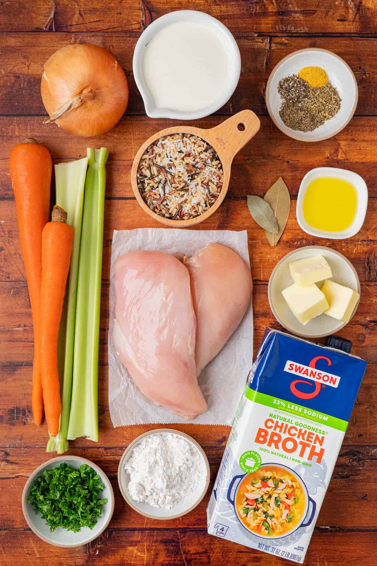 ingredient shot for creamy chicken and wild rice soup: onion rice, spices, carrots, celery, chicken, chicken broth, butter, bay leaf, flour, heavy cream.