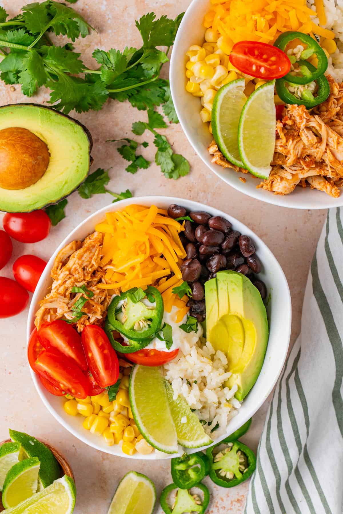 Two serving bowls filled with rice, chicken, avocado, beans, corn and tomatoes