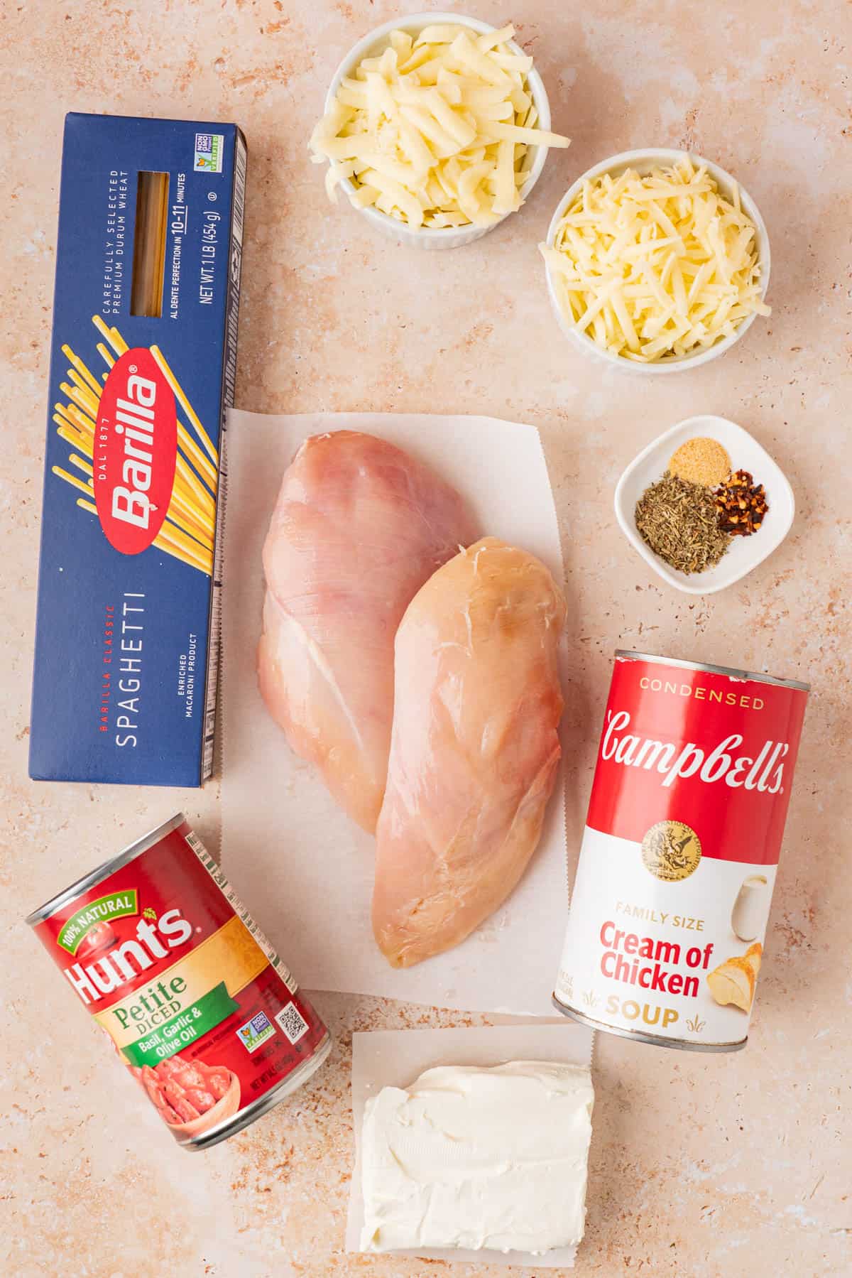 the ingredients for the chicken spaghetti pasta are pictured as 2 chicken breast, canned cream of chicken sou, spices, cheeses, cream cheese, box of pasta and canned tomaotes