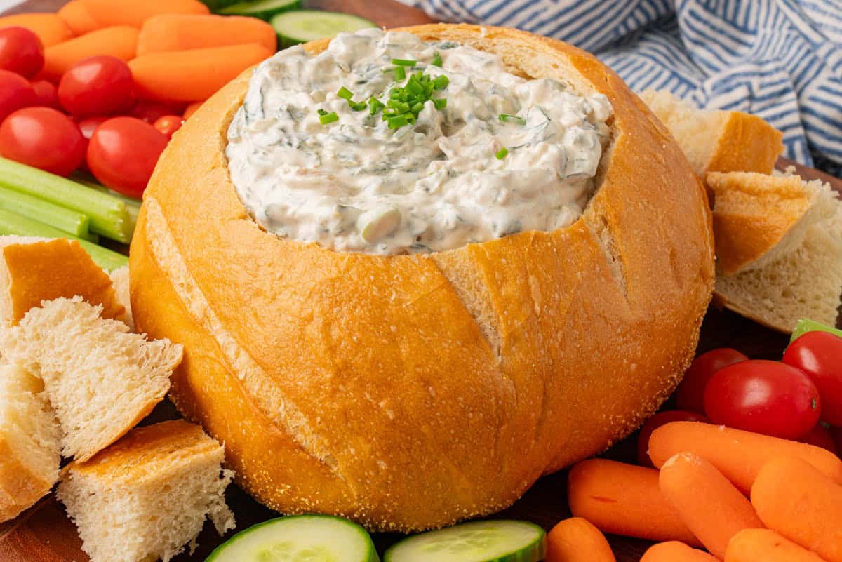 A landscape shot of Knorr's Spinach Dip in a bread bowl with vegetables and bread.