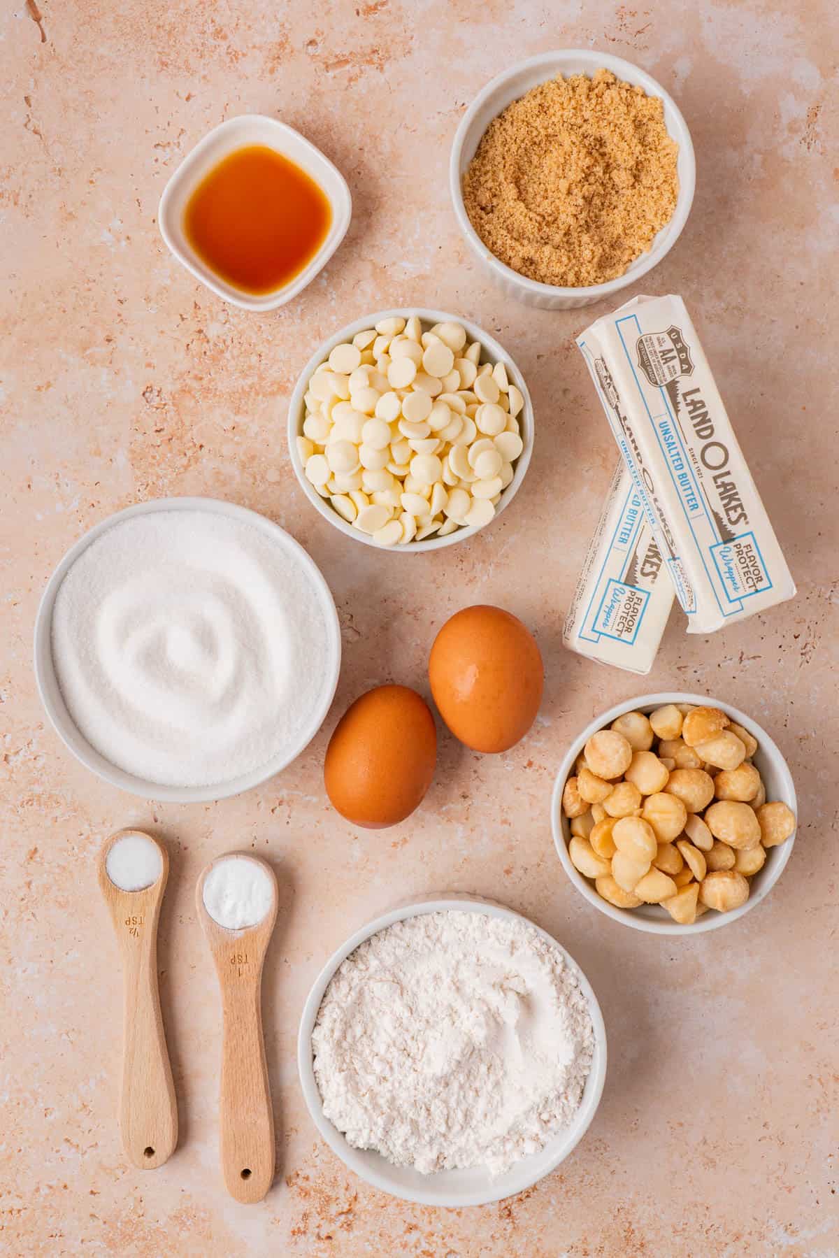 The ingredients for the cookies are butter, flour, salt, baking soda, brown sugar, white sugar, vanilla extract, white chocolate chips, eggs and macadamia nuts