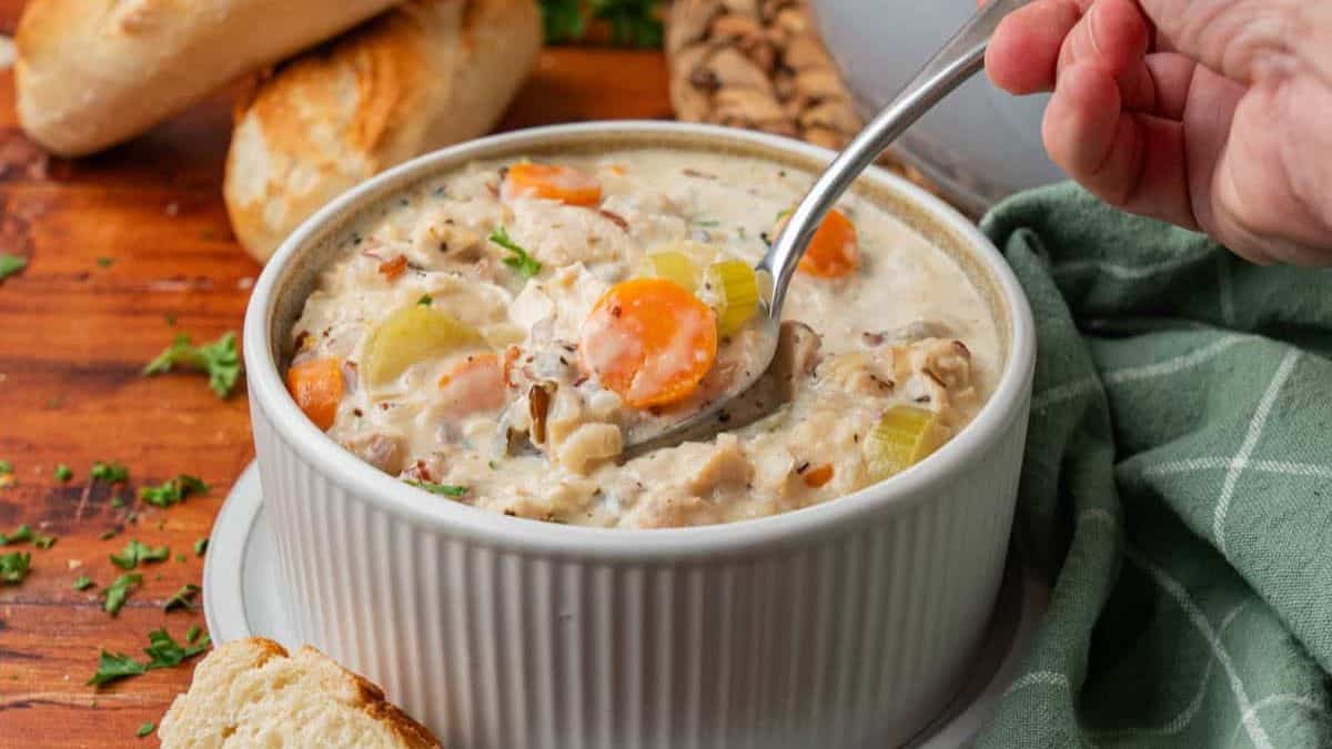 A serving of Chicken and Wild Rice served in a white bowl, and a clear spoonful is being fetched form the bowl of soup.