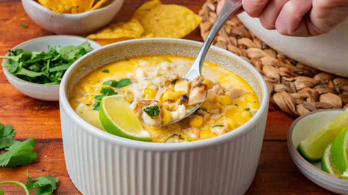 A white bowl filled with Mexican corn soup and a spoonful held by a hand.