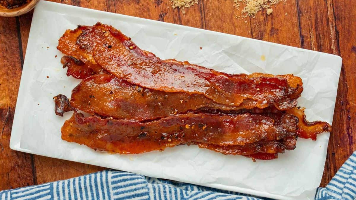 A few pieces of Candied Bacon served in a rectangular white plate. 