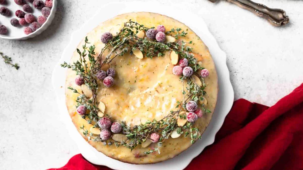 Top shot of a cake resting on a white cake stand topped with sugared cranberry wreath. 