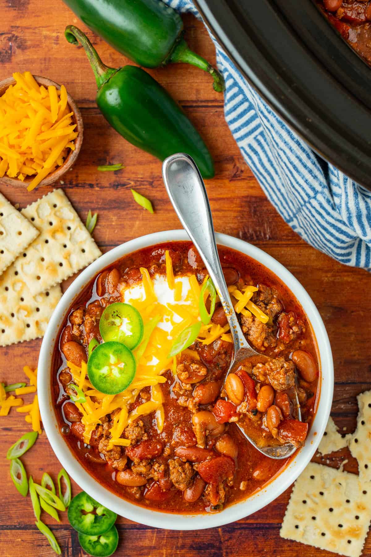 Overhead shot of a bowl of chili, fully garnished with jalapenos, cheese and sour cream. 