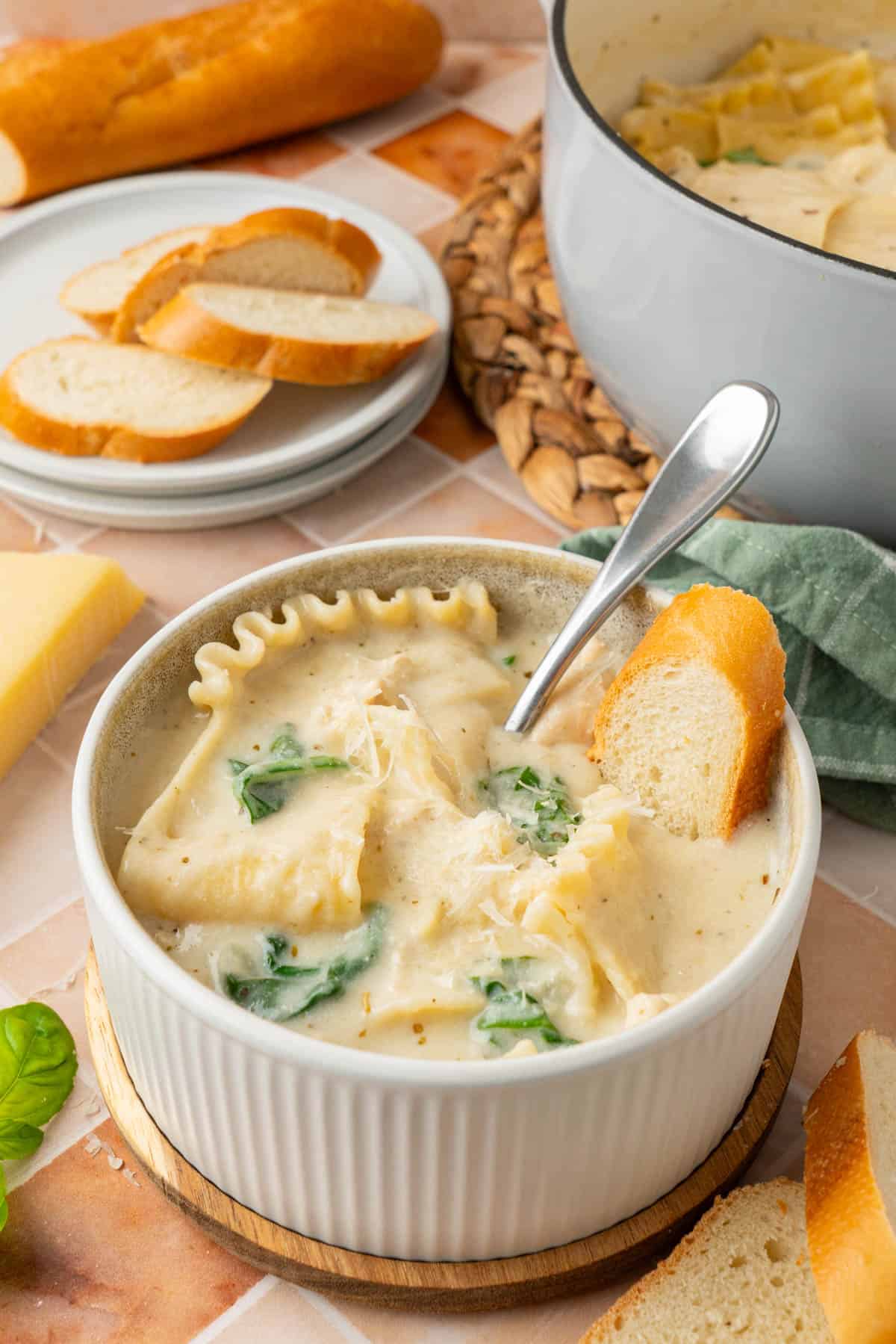 A bowl of white lasagna soup with sliced baguette dip on it.