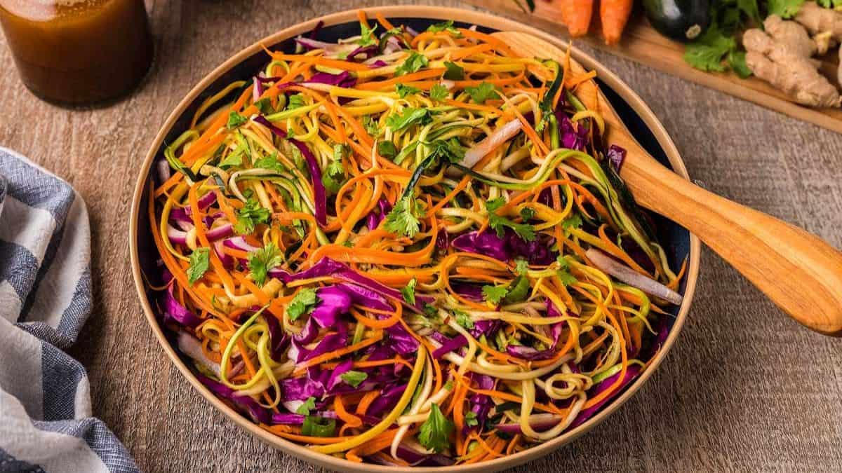 A serving bowl with a wooden spoon, filled with Asian Zoodle Salad. 