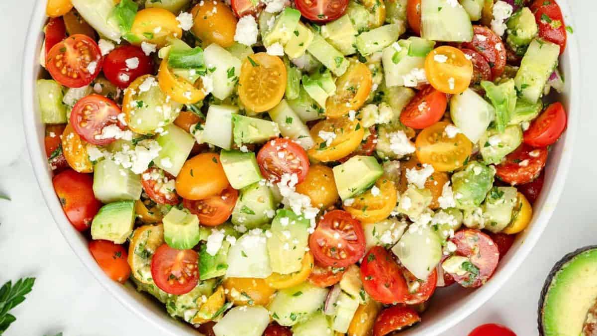 A top shot of a white serving bowl filled with Cucumber, Tomato and Avocado salad. 