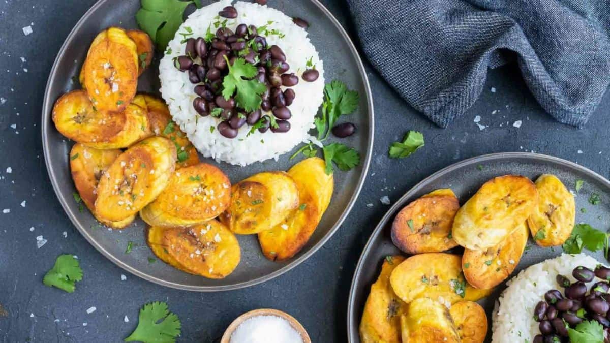 Two plate served equally with white rice topped with beans and some fried slices of plantain on the side.