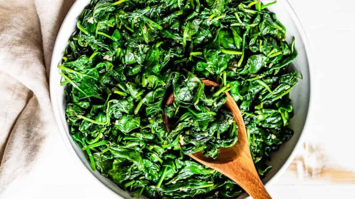 A plateful filled with garlic sauteed spinach and a wooden spoon on the side.