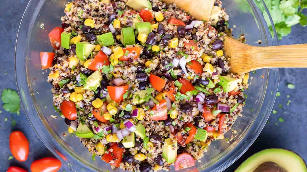 A clear bowl filled with Mexican Quinoa Salad with Avocado with wooden spoons on the side. 