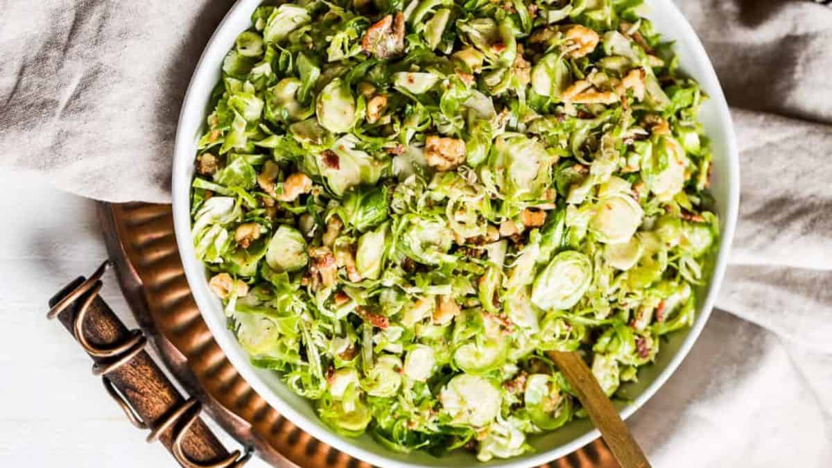 A top shot of a white serving bowl filled with Shredded Brussels Sprouts Salad with bacon Vinaigrette.