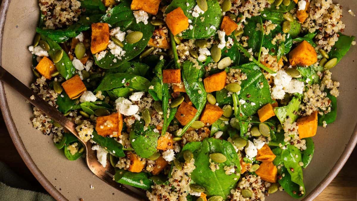 A bowl filled with warm spinach salad with quinoa and sweet potato.