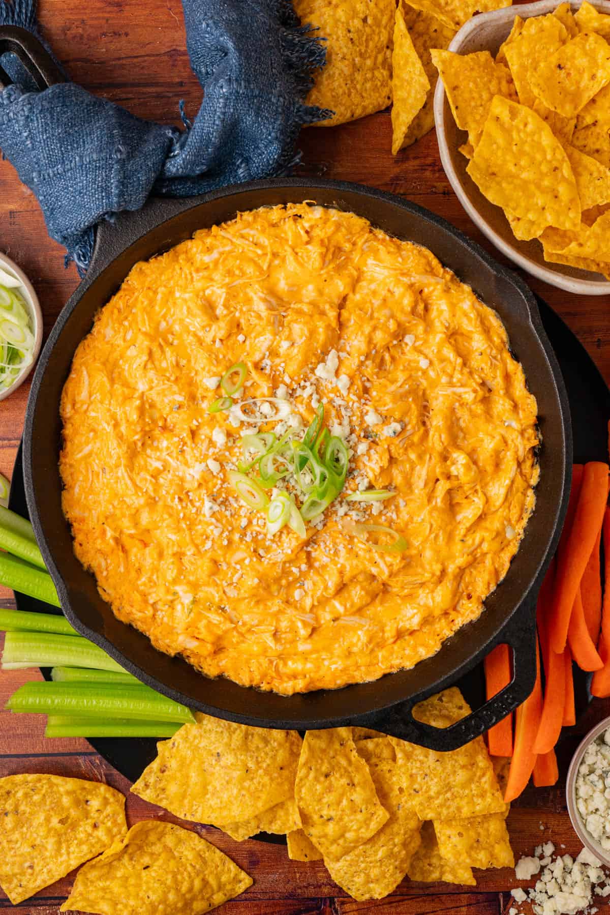 Buffalo chicken dip in a cast iron with celery and carrot sticks.