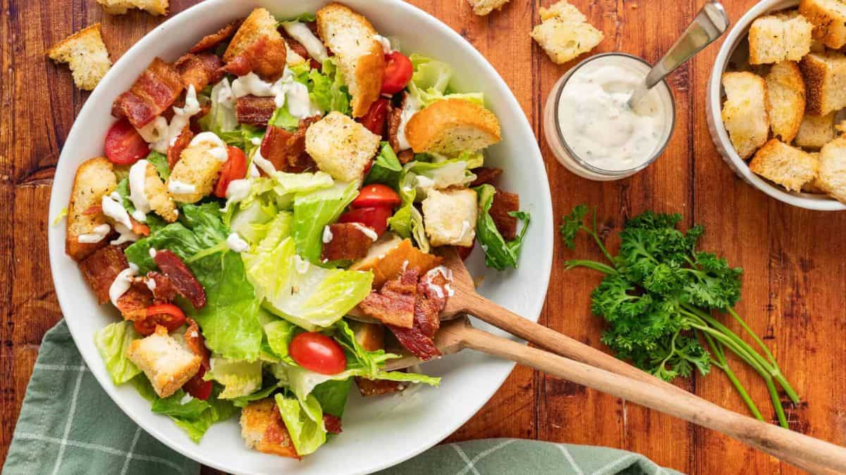 A bowl of salad with two wooden spoons.