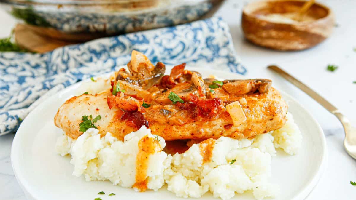 A plate of mashed potatoes topped with Bacon Mushroom Chicken.