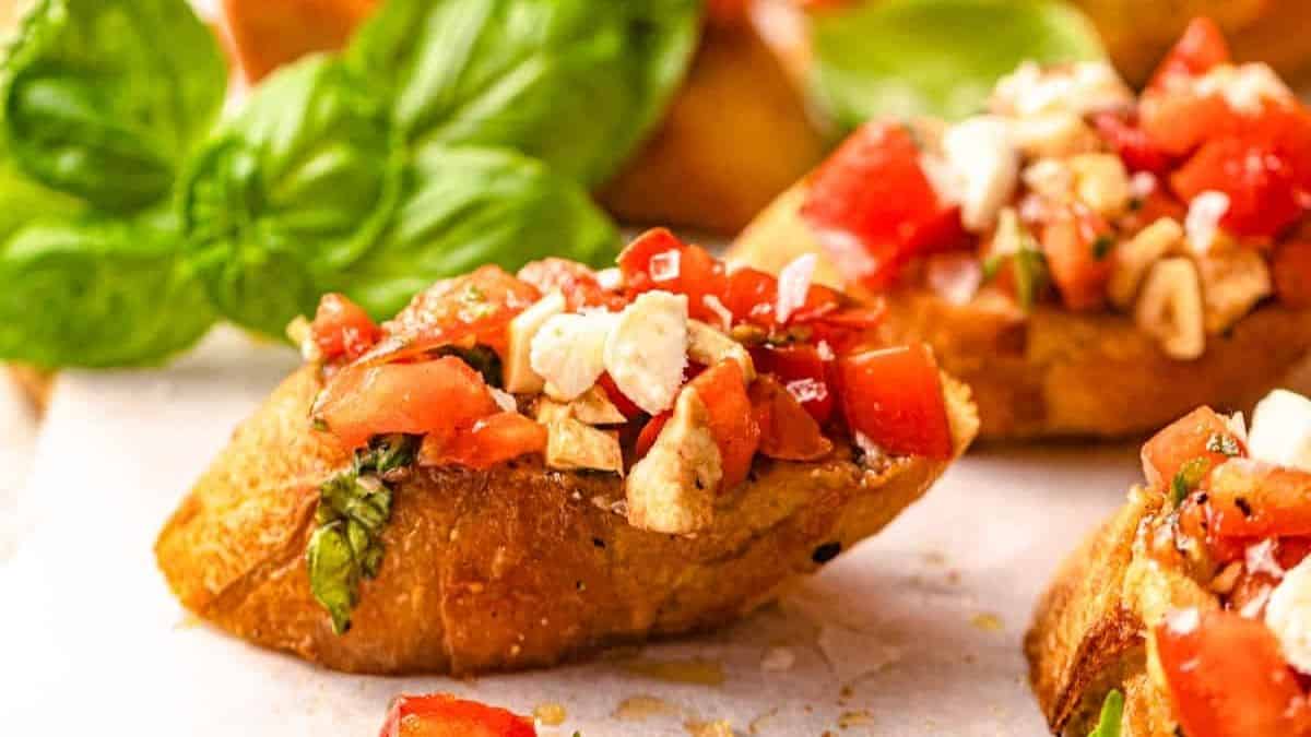 A close-up shot of a bruschetta with mozzarella and a few other pieces can be seen from the sides and blurry from the back. 