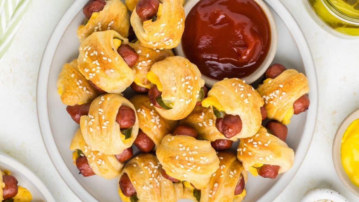 A top shot of a plateful of Cheeseburger Pigs in a blanket, and a ketchup dip on the side.