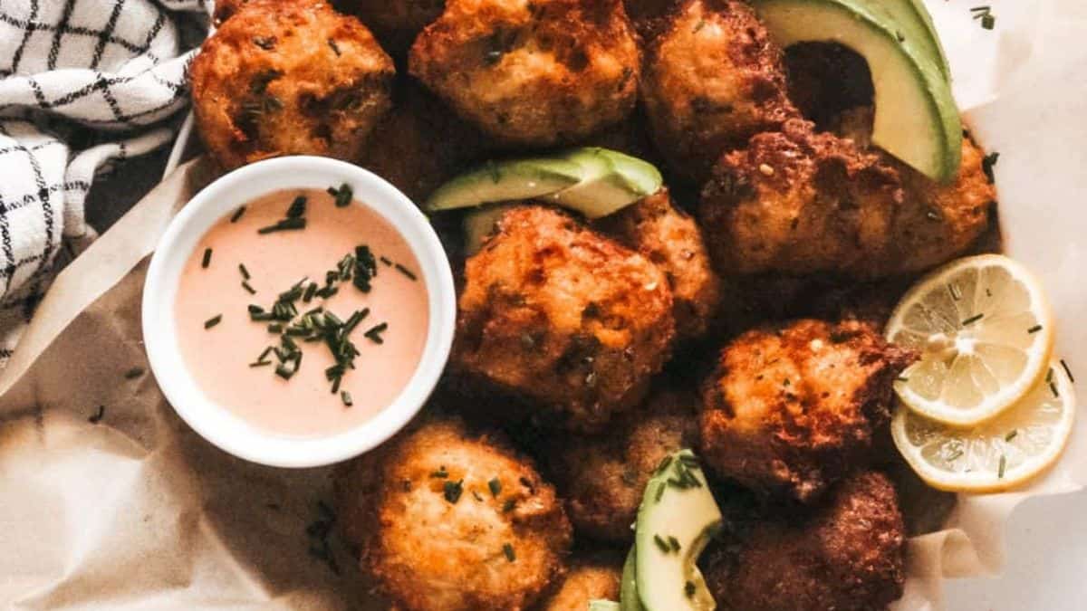 A close-up shot of cauliflower bites, with a side dip, a couple of slices of avocado and lemons respectively. 