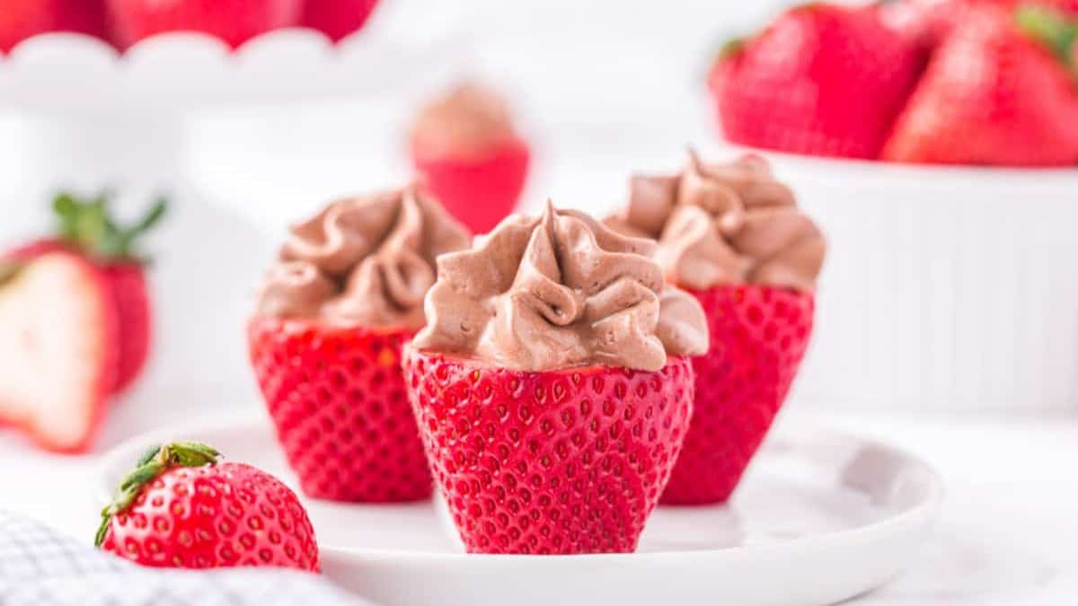 Three strawberries filled with chocolate cream cheese set on a plate. 