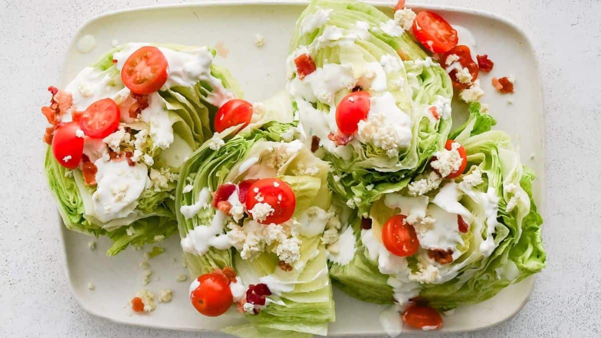 A top shot of a serving plate with four cabbage wedges topped with tomatoes, cheese crumbs.